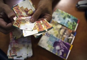 A bank employee counts Israeli Shekel notes for the camera at a bank branch in Tel Aviv